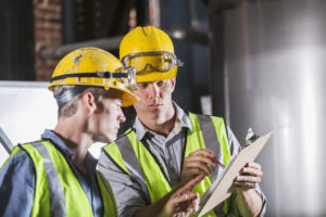 Two men wearing hardhats, vests and safety glasses